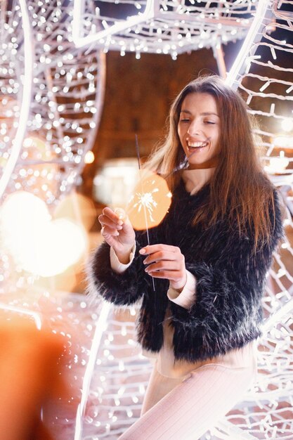 Portrait of young woman posing near white Christmas lighting