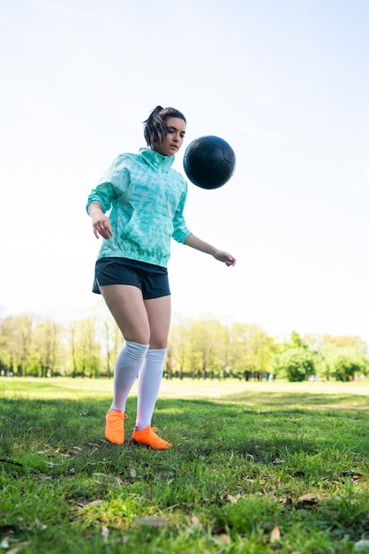 Portrait of young woman practicing soccer skills and doing tricks with the football ball. Soccer player juggling the ball. Sports concept.