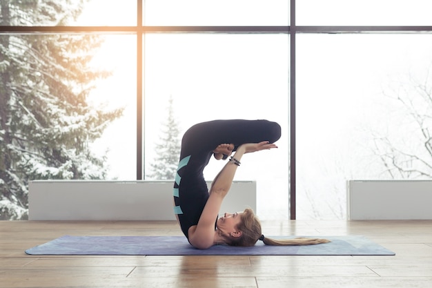 Portrait of young woman practicing yoga indoor near big window