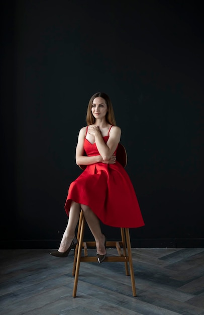 portrait of a young woman in a red dress sitting on a high bar stool