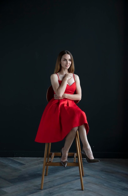 portrait of a young woman in a red dress sitting on a high bar stool