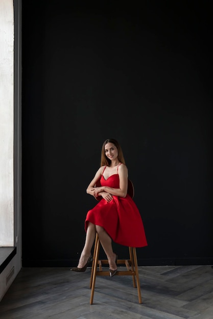 portrait of a young woman in a red dress sitting on a high bar stool