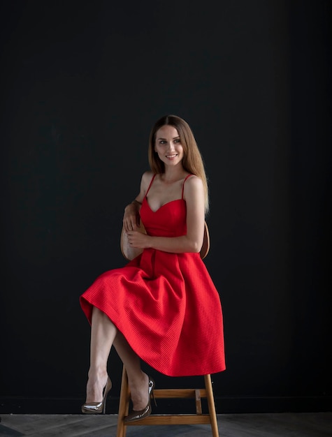 portrait of a young woman in a red dress sitting on a high bar stool