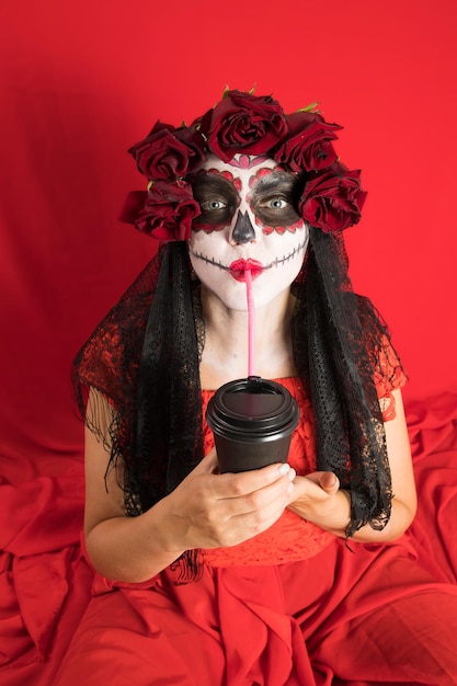 Portrait of a young woman in a red dress and traditional sugar skull makeup for the celebration of Dia de los Muertos the Day of the Dead