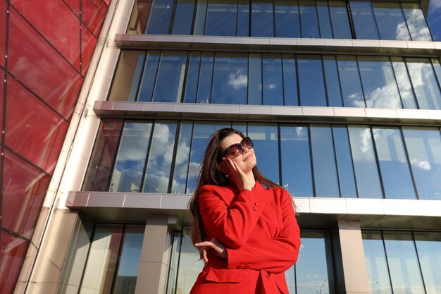 Portrait of a young woman in a red jacket on the background of glass buildings