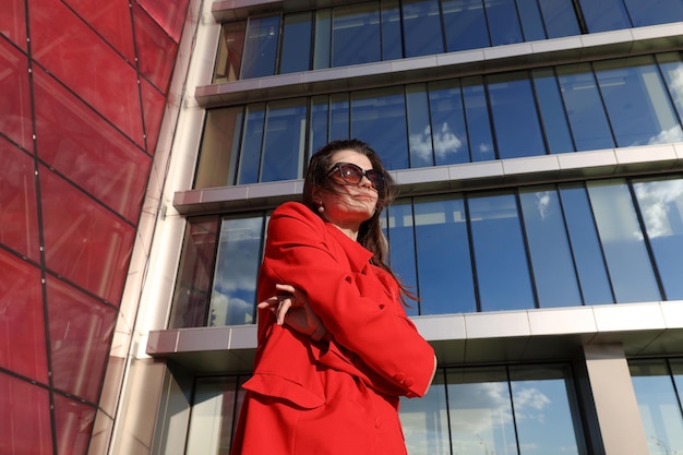 Портрет молодой женщины в красной куртке на фоне стеклянных зданий