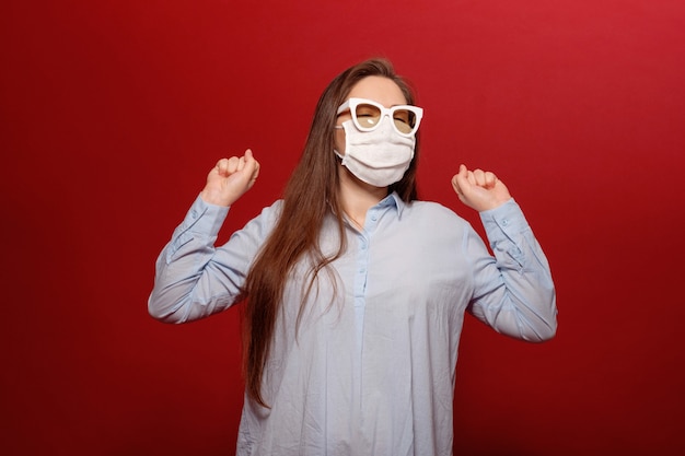 Foto ritratto di giovane donna sulla parete rossa in maschera protettiva medica e occhiali da sole