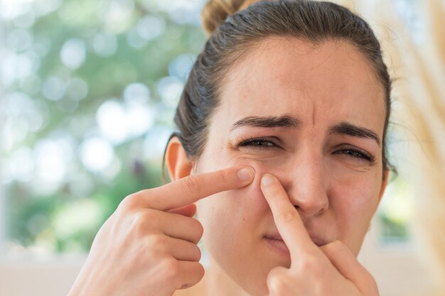 Portrait of young woman removing a pimple on her face and with a pain expression