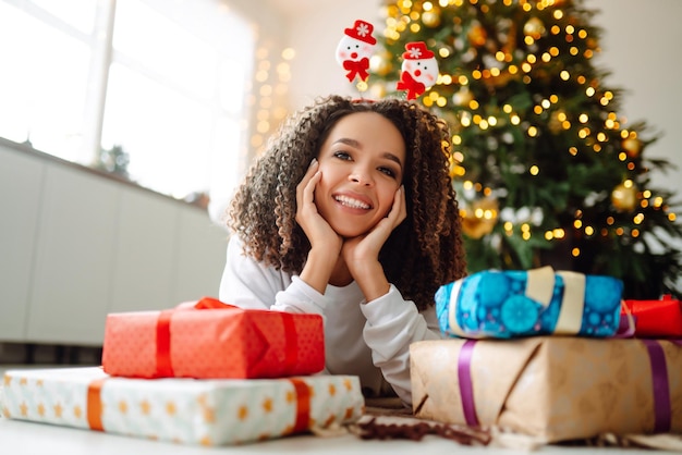 Portrait of young woman in santa claus hat with gift at the Christmas tree Christmas New year's