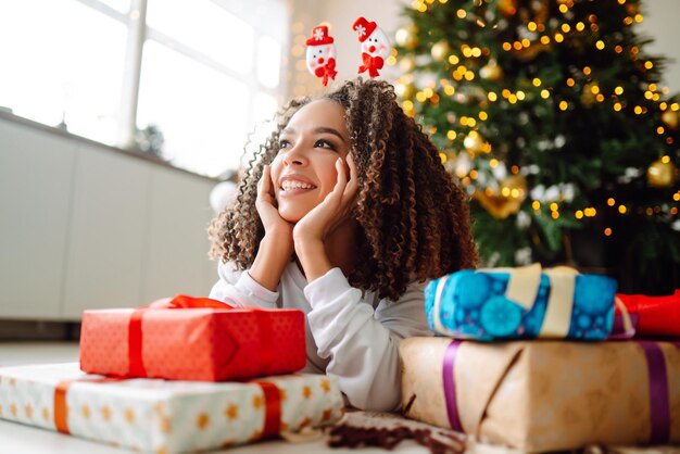 Portrait of young woman in santa claus hat with gift at the Christmas tree Christmas New year's