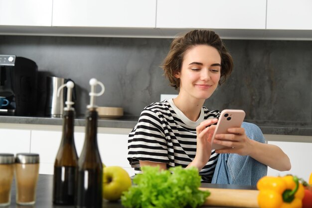 Photo portrait of young woman searching for cooking recipes online using smartphone sitting near