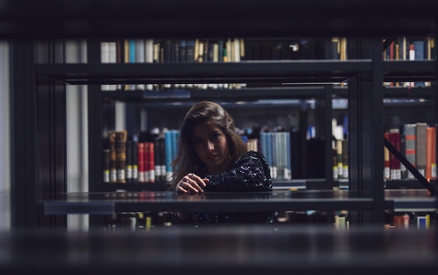 portrait of young woman seen through bookshelves at library