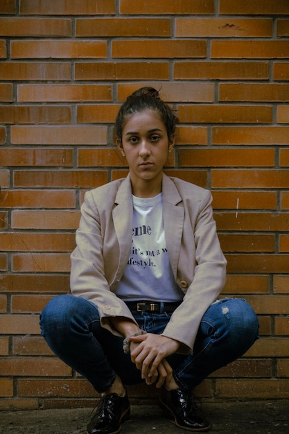 Photo portrait of young woman sitting against brick wall