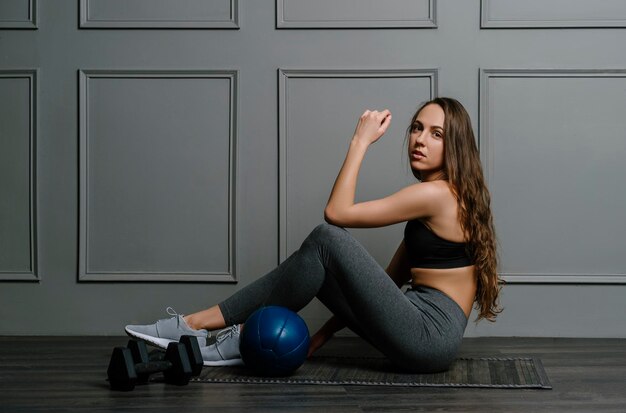 Портрет молодой женщины, сидящей у медицинского мяча на стене