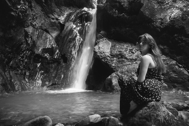 Foto ritratto di una giovane donna seduta accanto a una cascata su una roccia