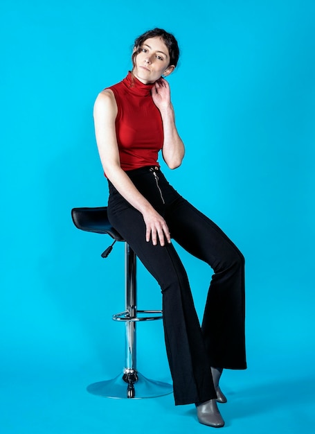 Portrait of young woman sitting on chair against blue background