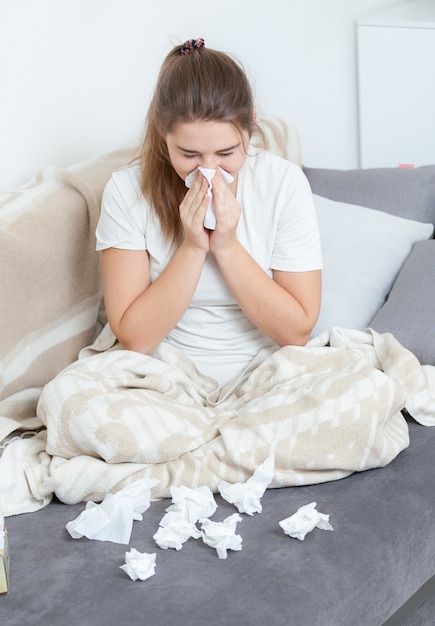 Portrait of young woman sitting on couch and blowing nose