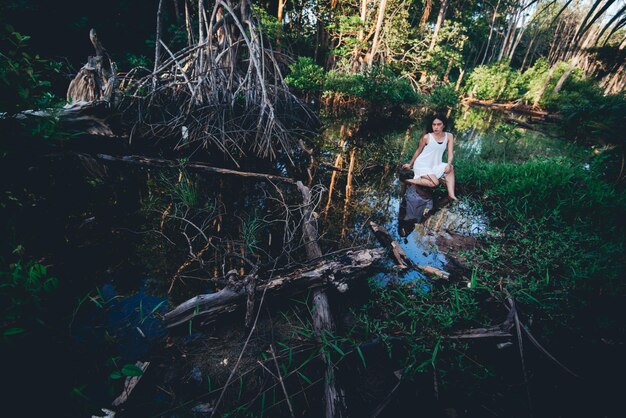 Foto ritratto di una giovane donna seduta sul legno galleggiante sopra un ruscello nella foresta