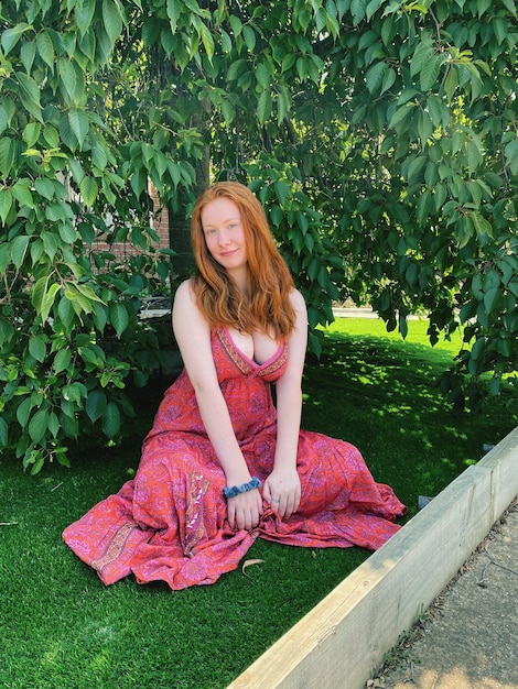 공원 의 나무 에 맞서 잔디 에 앉아 있는 젊은 여자 의 초상화