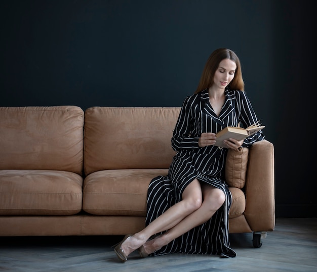 портрет молодой женщины, сидящей на диване у окна и читающей книгу