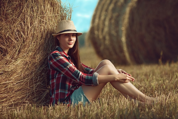 Photo portrait of young woman sitting next to a stack of hay in sunlight