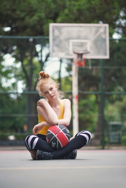 Foto ritratto di una giovane donna seduta con la pallacanestro in un campo sportivo