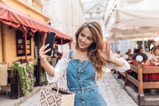 Portrait of young woman smiling broadly while holding smartphone strolling outdoor