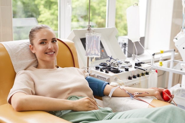 Ritratto di giovane donna che sorride alla macchina fotografica mentre sdraiato sul divano e donando il sangue in ospedale