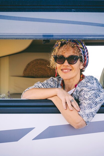 Portrait of young woman smiling at the camper van window Happy tourist enjoy travel vanlife lifestyle Renting rv caravan for vacation leisure Caucasian female cheers and enjoy holiday destination