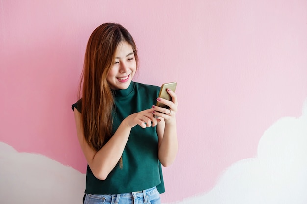 Portrait of Young Woman Smiling while using Smart Phone at the wall