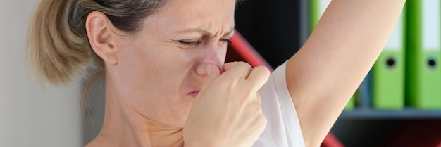 Foto ritratto di giovane donna che annusa le ascelle e copre il naso igiene e concetto di assistenza sanitaria