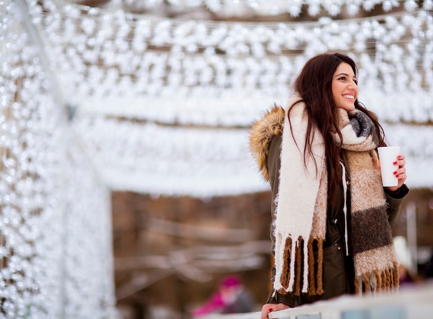 Portrait of young woman in a snow park drinks tea at Christmas market