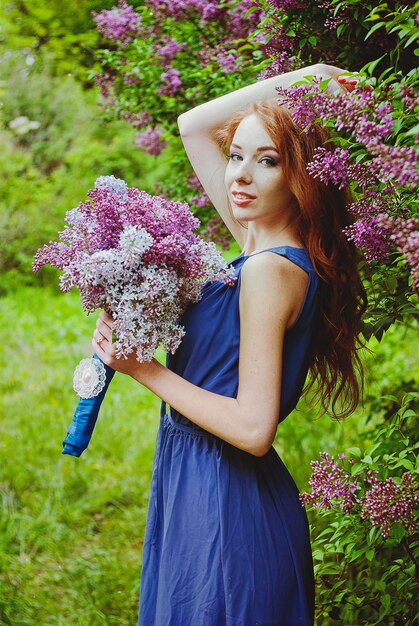 Portrait of young woman in spring garden with freckles. blooming purple flowers. Lilacs bouquet