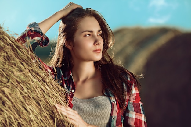 Portrait of young woman next to a stack of hay in sunlight