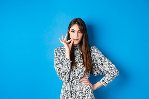 Portrait of young woman standing against blue background