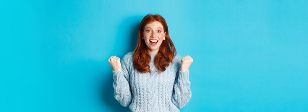 Portrait of young woman standing against blue background