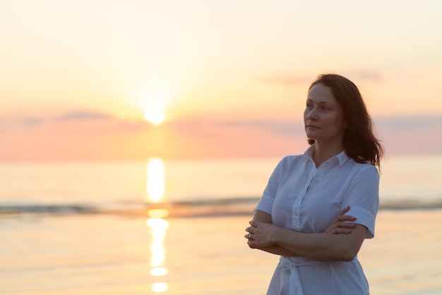 Portrait of young woman standing against sea during sunset