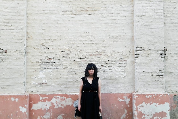 Portrait of young woman standing against wall