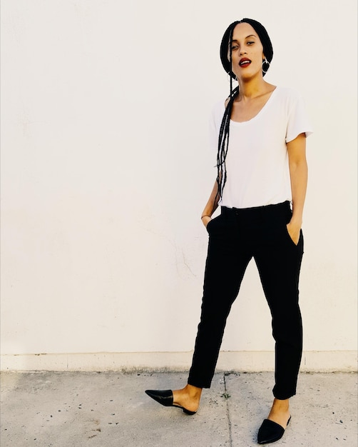 Portrait of young woman standing against white wall