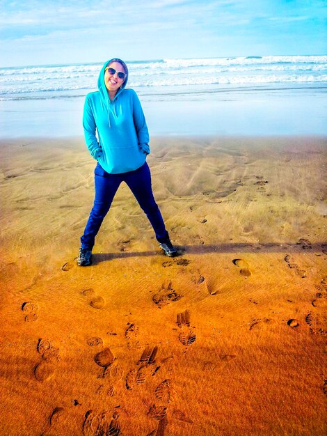 Portrait of young woman standing on beach against sky