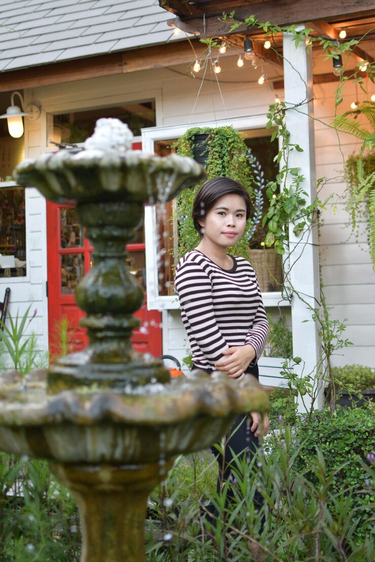 Photo portrait of young woman standing by fountain and plants against house
