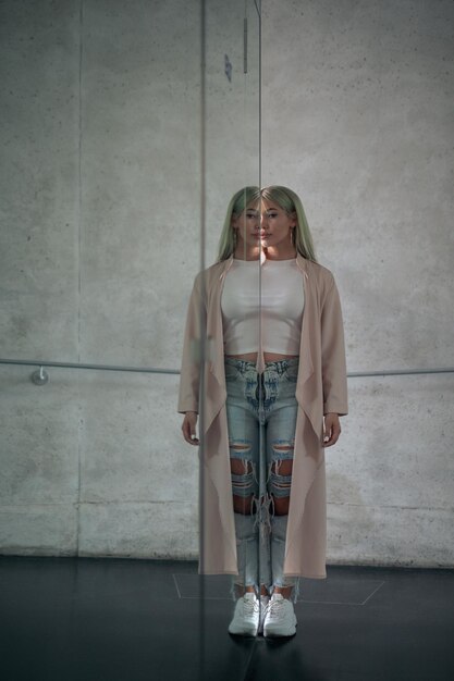 Portrait of young woman standing by mirror with reflection against wall