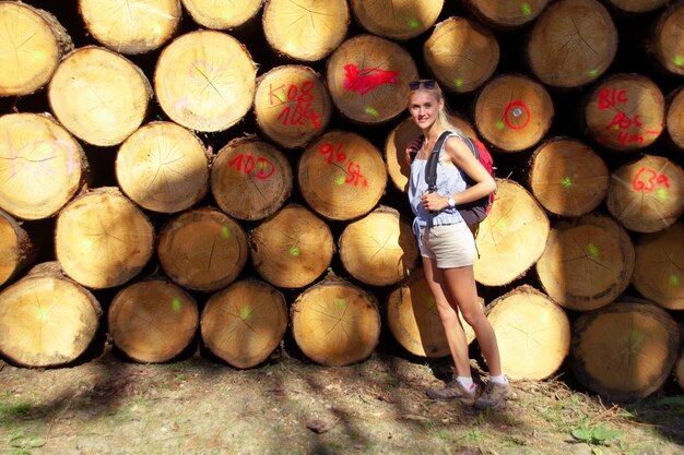 Portrait of young woman standing by stacked logs