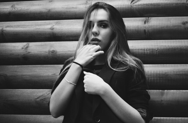 Portrait of young woman standing by wooden wall