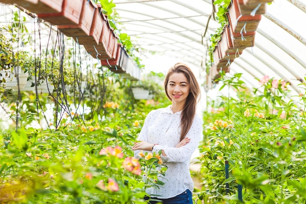 Ritratto di una giovane donna in piedi in una serra con bellissimi fiori e sorridente