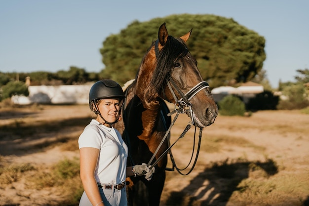 Portrait of a young woman standing next to her brown horse