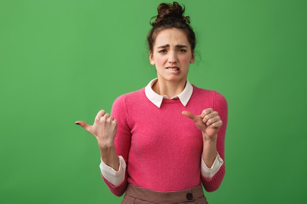 Portrait of a young woman standing isolated, pointing at copy space