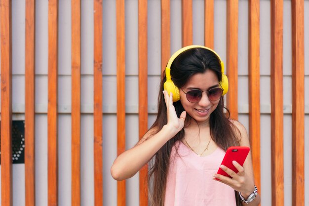 Portrait of a young woman standing smiling with a smartphone and listening to music.