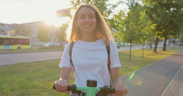 Portrait of young woman standing with escooter on street and posing for camera