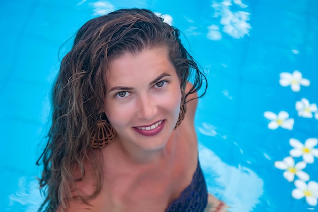 Portrait young woman in swimsuit looking at camera in blue swimming pool